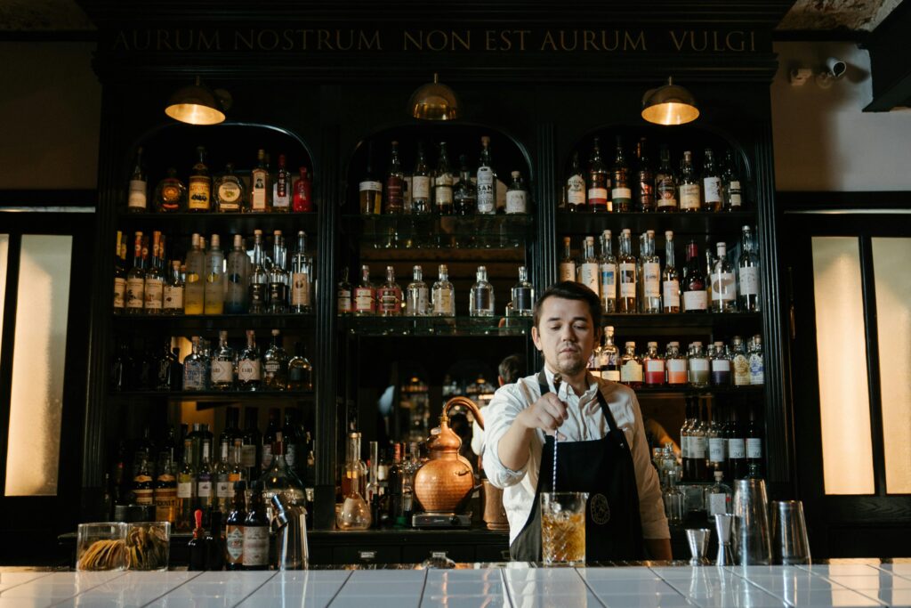 Bartender skillfully mixing a cocktail in a stylish bar with shelves of assorted bottles.